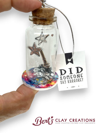 Decorative bottle with star and microphone charm, held by a hand, on a white background with 'Bert's Clay Creations' branding.